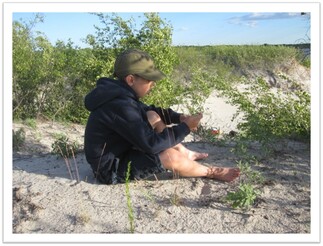 kid sitting on sand with greenery around him